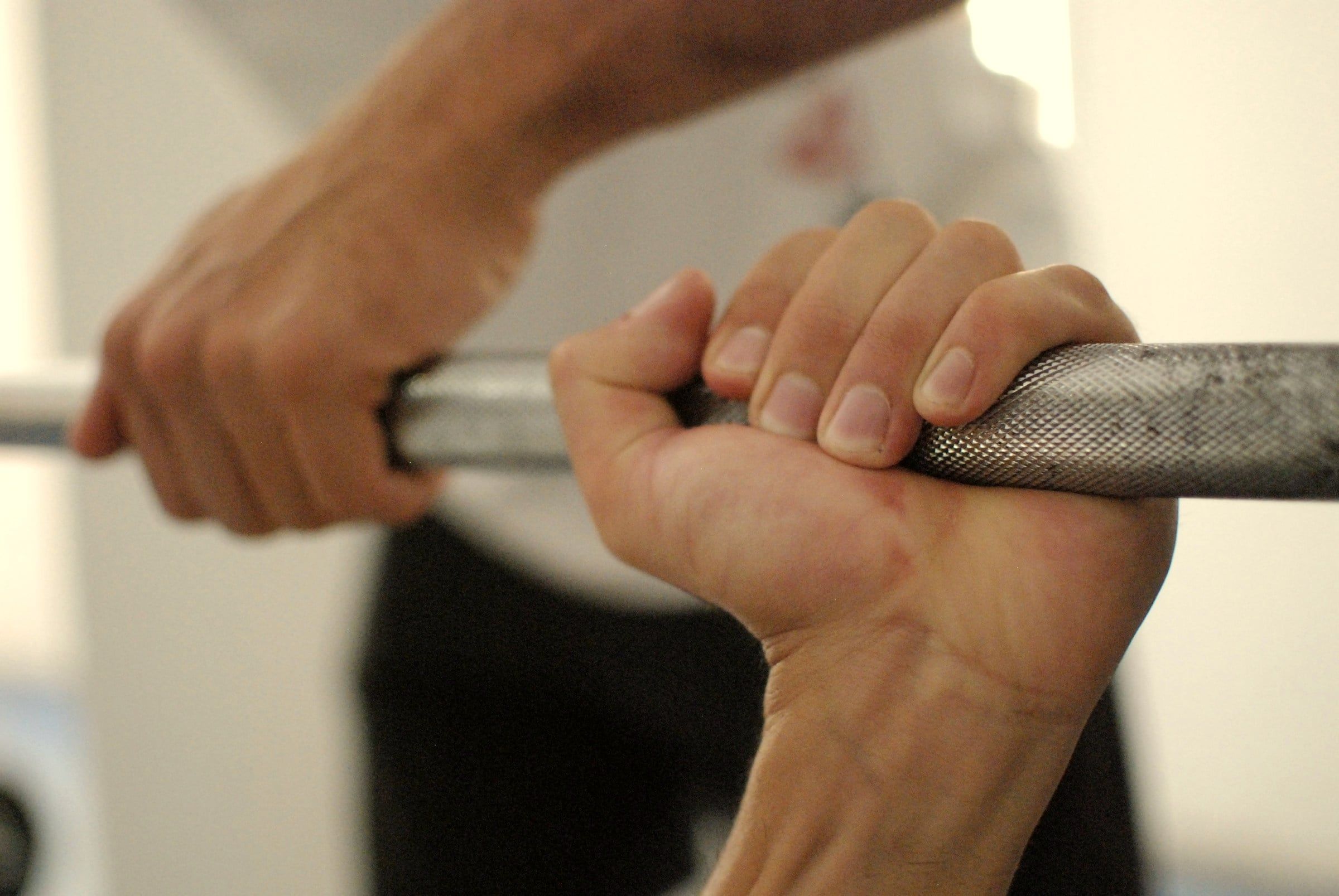 Two hands take an overhand grip on the knurled part of a barbell.