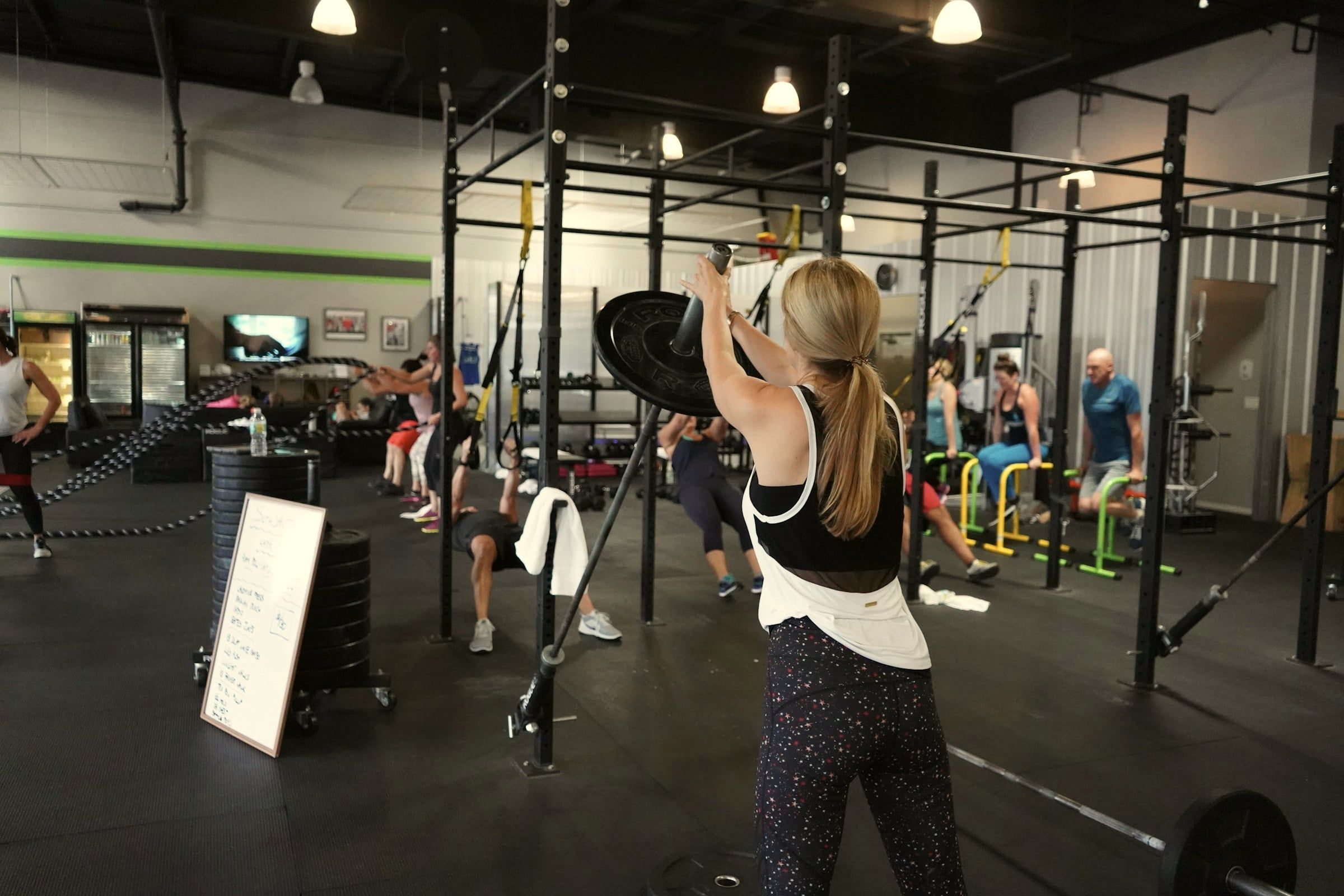 A small group trains at stations around a rig, one member pressing a barbell in front.